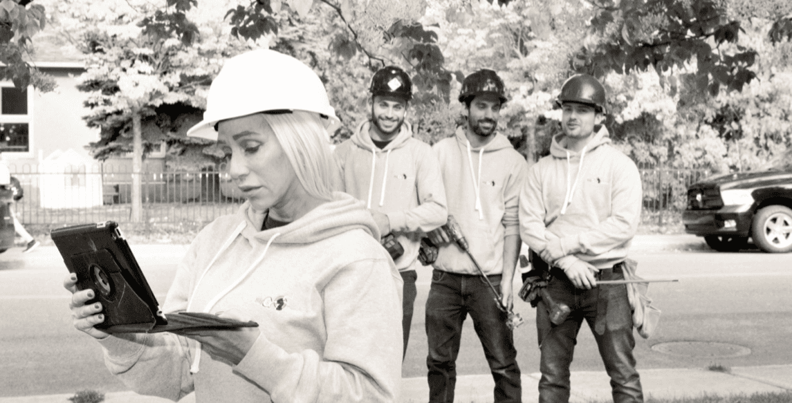 La propriétaire de Big G Electric, tenant une tablette et portant un casque de sécurité, est debout avec son équipe de trois électriciens sur un chantier.